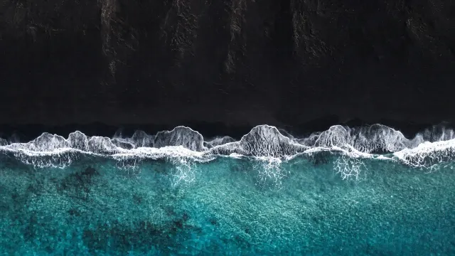 Aerial Turquoise Tide Breaking over Pristine Volcanic Black Sand